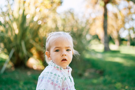 Little girl stands in a green garden with her mouth open