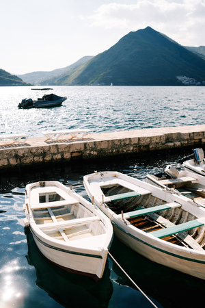 Fishing boats moored at an old stone pier with mountains in the backgroundの写真素材