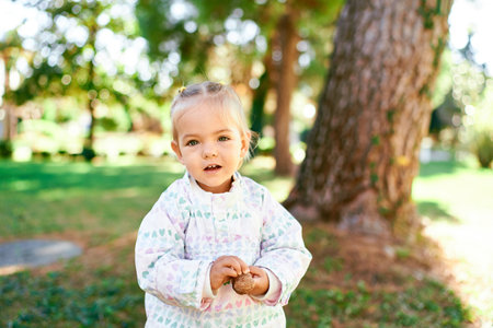 Little smiling girl stands near a tree in a sunny forest with something in her hands