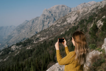 Young woman stands on a mountain and shoots a view with a smartphone. Side view