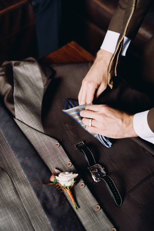 Groomsman folds a handkerchief on groom suit next to the boutonniere