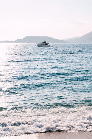 View from the shore to the yacht sailing on the sea against the backdrop of the mountainsの写真素材