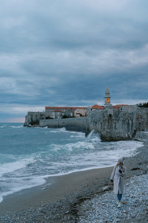 Traveler walks along the coast near the fortress walls of the ancient town of Budva, looking at the sea. Montenegroの写真素材