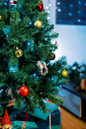Figurine of a horse on skids hangs on a branch of a Christmas tree among colorful balls