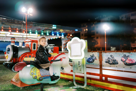 Little girl sits on an electric rocking horse swing at a fair and looks awayの写真素材