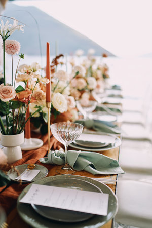 Knotted napkins lie next to a plate with a festive menu and bouquets of flowers on a table by the...