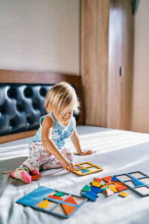 Little girl puts together a puzzle on the bedの写真素材