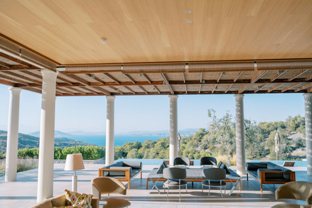Lounge area with armchairs and sofas on a terrace with columns by the pool. Peloponnese, Greece