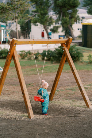 Little girl holds the swing seat behind her to sit on. Back viewの写真素材