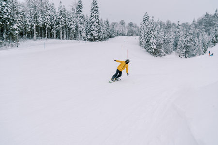 Snowboarder in a yellow ski suit rides a snowboard leaning to the side from a snowy mountainの写真素材