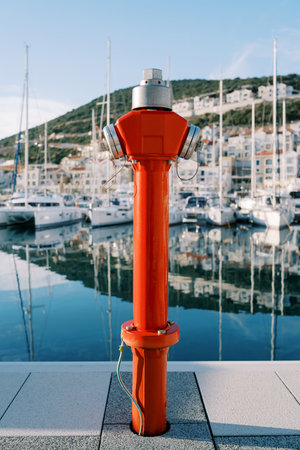 Red fire hydrant stands on a pier with moored yachtsの写真素材