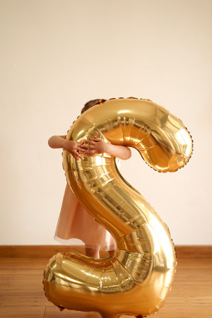 Little girl is standing in a room hugging an inflatable number 2の写真素材