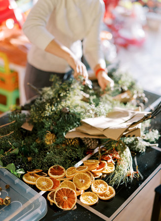 Designer makes a New Year wreath from coniferous branches, pieces of dried oranges and cones on the...