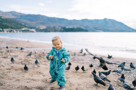 Little smiling girl walks along the seashore among a flock of pigeonsの写真素材