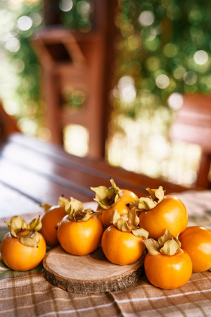 Ripe persimmon lies on a wooden board on a checkered napkin on a table in the gardenの写真素材
