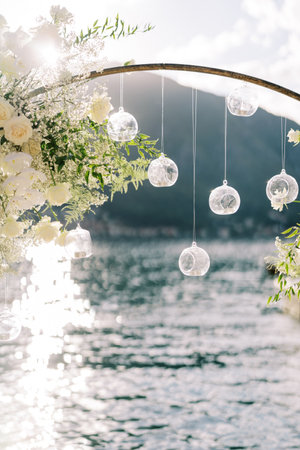 Tablet candles in round ball-candlesticks hang from a wedding arch standing by the seaの写真素材