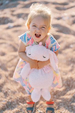 Little girl standing on the beach hugging a toy hare. Top viewの写真素材