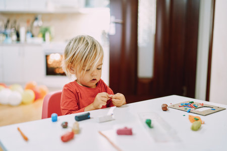 Little girl sits at a table and sculpts from plasticineの写真素材