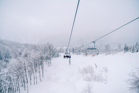 Skiers ride over snow-capped mountains on a four-seater chairliftの写真素材