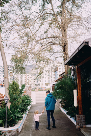 Mom and a little girl are standing in the park against the backdrop of high-rise buildings holding...