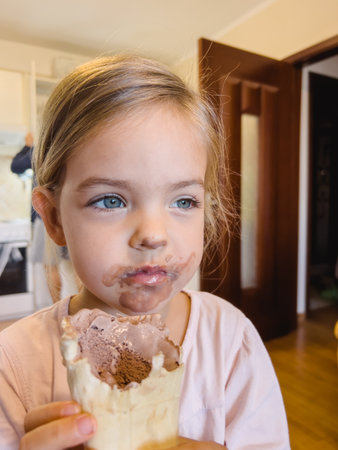 Little girl with a dirty face sits with chocolate ice cream in a waffle cupの写真素材