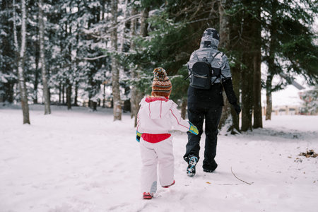 Little girl follows her mother through snowdrifts in a snowy forest. Back viewの写真素材