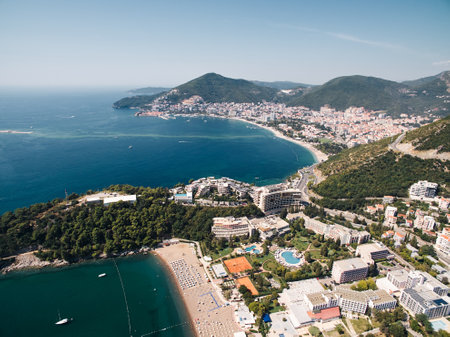 Sandy beach by the sea opposite hotels with swimming pools at the foot of the mountains. Budva, Montenegro. Droneの写真素材