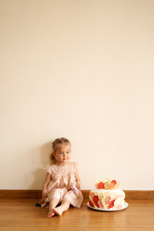 Little smiling girl sits on the floor next to a birthday cakeの写真素材
