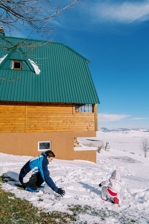 Dad with a small child making a snowman near a wooden cottage. Back viewの写真素材