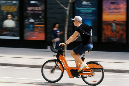 Toronto, Canada - May 26, 2026: Young Man Riding Orange Bike Share Bicycle Past Theatre Posters