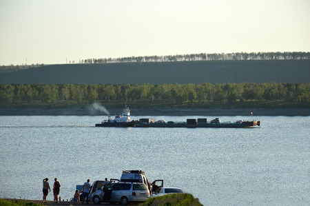 The ferry passes across the river cars and people. People are waiting for the ferry on the shore.の写真素材