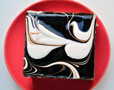 Black and white Square on red Round. Light background. Cake with icing on the plate. Close-upの写真素材