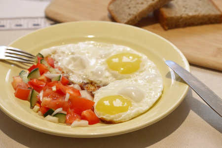 Fried eggs with tomatoes and cucumbers on a plate with breadの写真素材