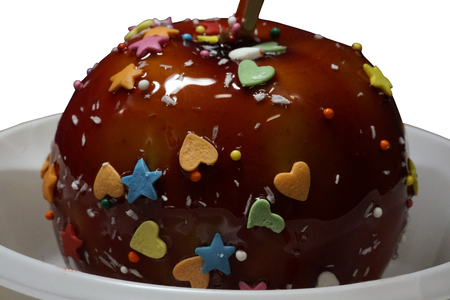 Apple in a caramel glaze. Strew of hearts stars balls. Apple close-up in white plate isolated on white background. Food.の写真素材