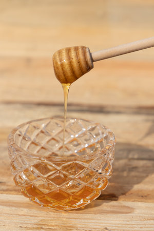 glass bowl with honey and honey dipper on a wooden table