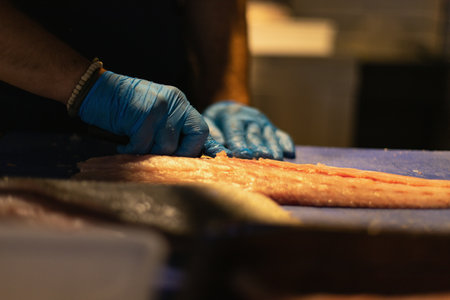 the chef cuts the fish in blue gloves