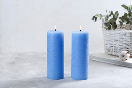 Blue candles, beautiful green flowers in a basket. Light gray textured background.の写真素材