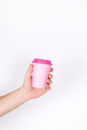 Breakfast and coffee theme: man's hand holding white empty paper coffee cup with a brown plastic cap...