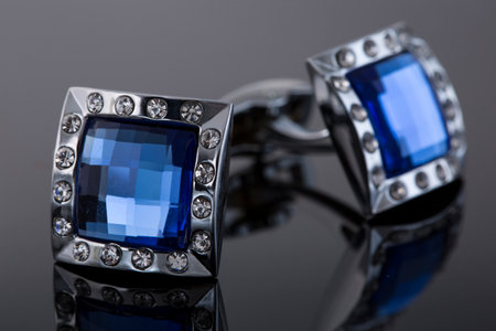 Two cufflinks made of white metal with blue stones on a black background