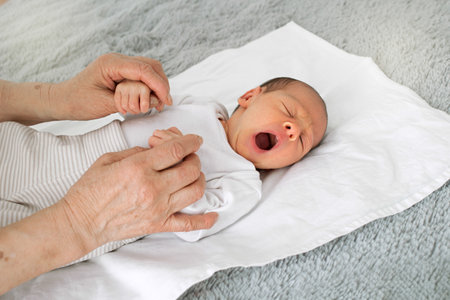 A newborn baby smiles very cute. Grandmother holds the baby by the handles. Very funny baby yawns.