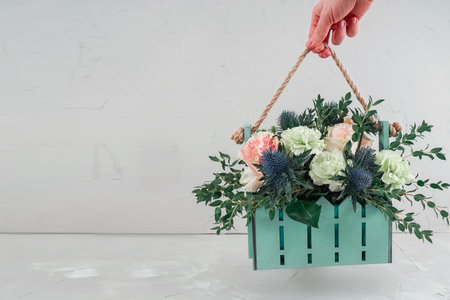 Beautiful bouquet in a basket. Hand holds a bouquet in a designer box. Gift bouquet for your girlfriend on March 8. Delicate roses in mint decoration on a gray background.の写真素材