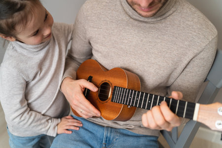 Dad plays the guitar with his daughter. The child learns to play a musical instrument with a tutor. Musical duet of a father with a childの写真素材