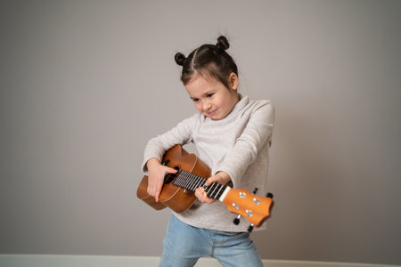 Little girl plays ukulele. Creative development in children. Musical education from childhood. Teaching music online at homeの写真素材