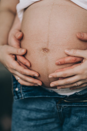 Belly of a pregnant girl close up. The hands of the guy and the girl on the stomach. Heart on the belly of a pregnant girlの写真素材