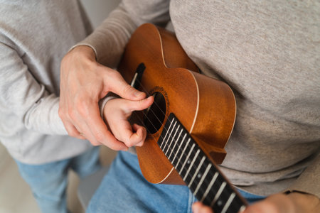 Dad teaches his daughter to play the ukulele. Home teaching to play the guitar. Close up of ukulele...
