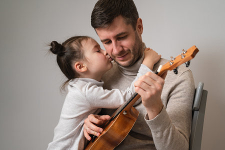 Dad plays the guitar with his daughter. The child learns to play a musical instrument with a tutor. Musical duet of a father with a childの写真素材