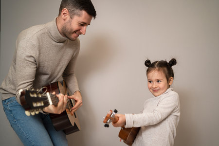 Dad plays the guitar with his daughter. The child learns to play a musical instrument with a tutor. Musical duet of a father with a child.の写真素材