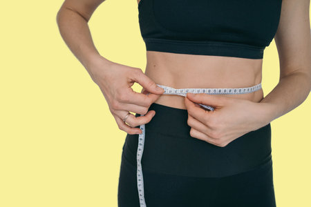 The girl measures her waist. Isolate with a girl in a sports black suit.
