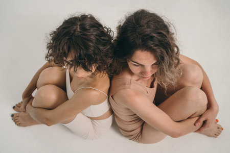 A beautiful girl with curly hair looks into the frame. A girl without makeup. A beautiful and natural woman. Minimalism in appearance. Two girls in their underwear are sitting next to each other.の写真素材