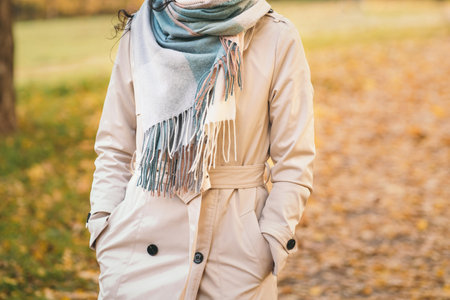 A girl in a beige cloak walks through the autumn park. The girl enjoys the autumn weather. Background with orange leavesの写真素材